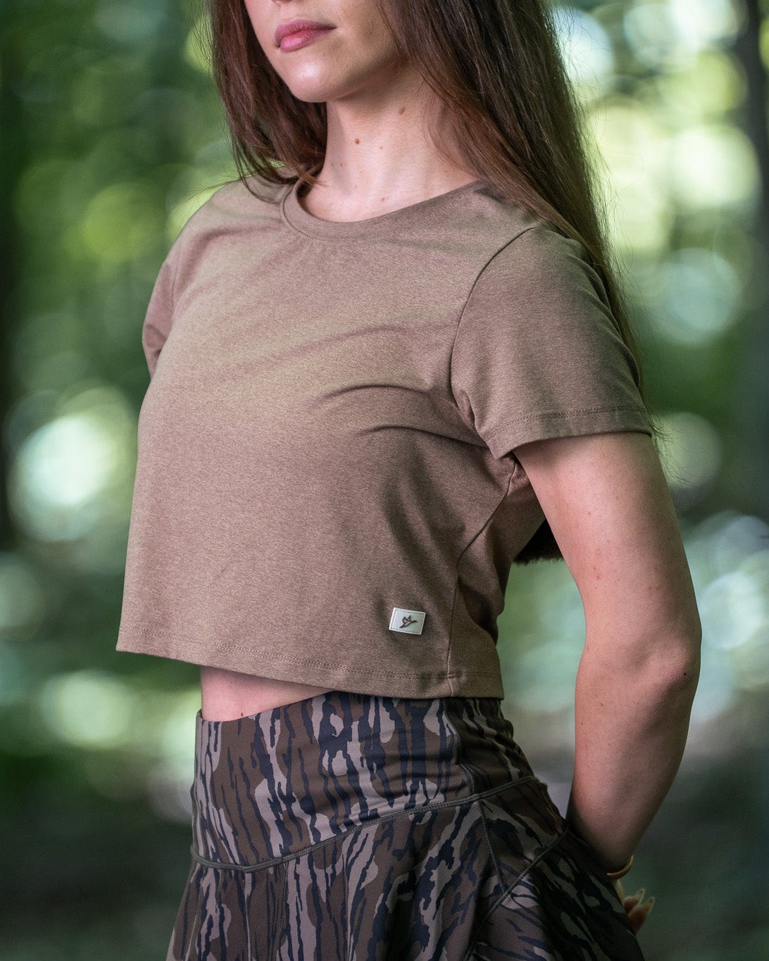 Woman wearing a brown t-shirt and patterned pants standing in a forest
