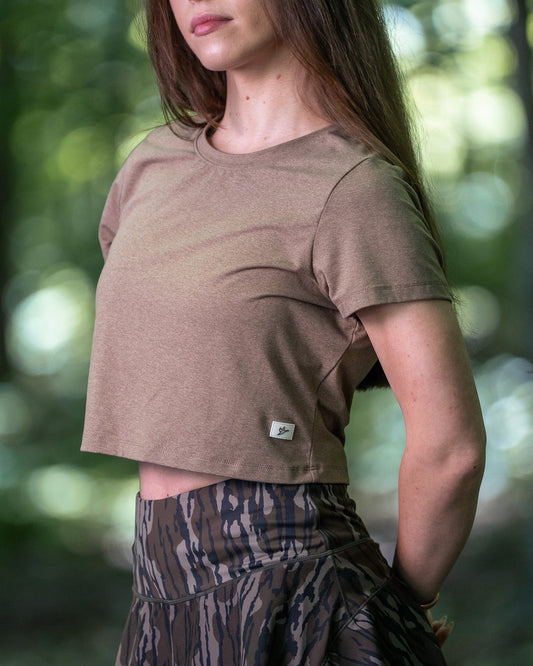 Woman wearing a brown t-shirt and patterned pants standing in a forest
