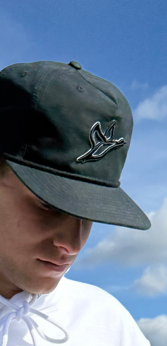 Person wearing a green cap with a logo against a blue sky