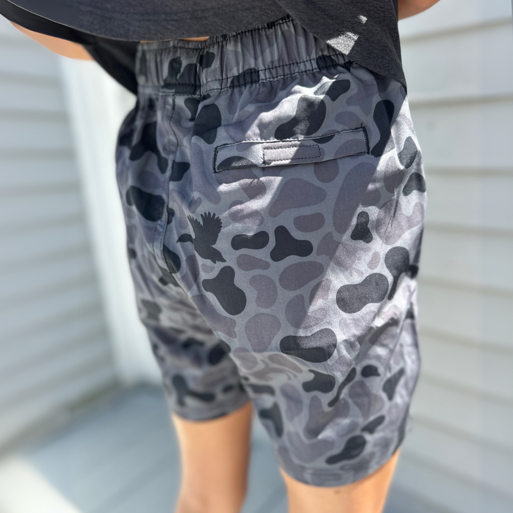 Youth person wearing the Committed Camo volley shorts in Kandahar Camo, a greyscale camo, with a neutral background.